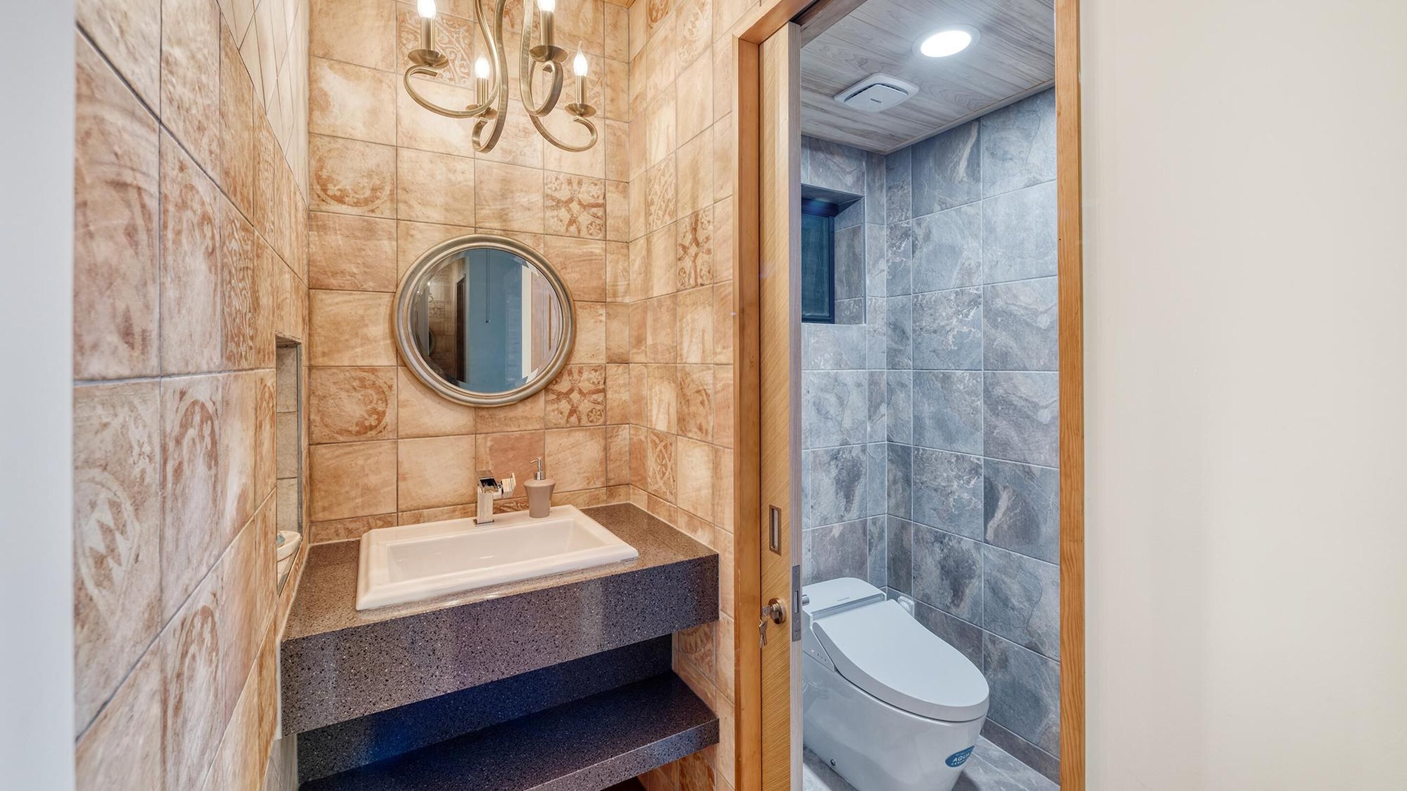 A bathroom with a marble vanity, a round mirror, a toilet, and a shower area.