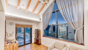 A spacious living room with a large window, wooden beams, a chandelier, and a view of the outdoors. - Seogwipo Hanonui Achim Pensiom (Seogwipo)