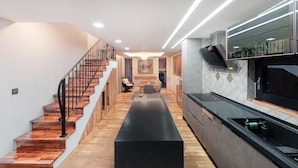 A modern kitchen with a black countertop, wooden staircase, and a dining area with a long table. - Seogwipo Hanonui Achim Pensiom (Seogwipo)