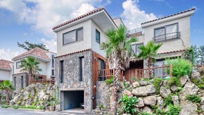 A two-story house with a stone facade, a wooden door, and a balcony with metal railings. - Seogwipo Hanonui Achim Pensiom (Seogwipo)