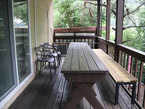 Eine Holzterrasse mit Picknicktisch und -stühlen, umgeben von einem Hollerdgeschoss und einer Glastür.
