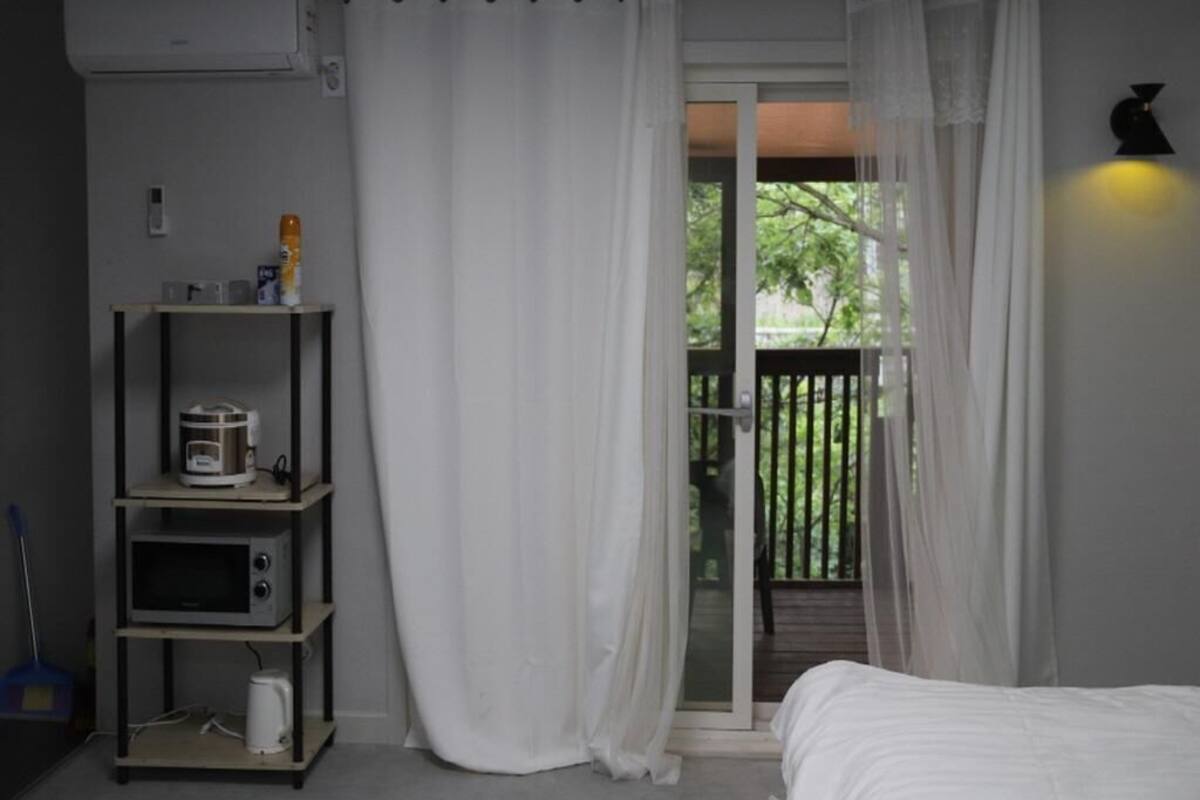 Ein Schlafzimmer mit einem Bett, einer Schiebetür zu einem Balkon, einer Ablage mit Küchengeräten und einer Wand-Klimaanlage.