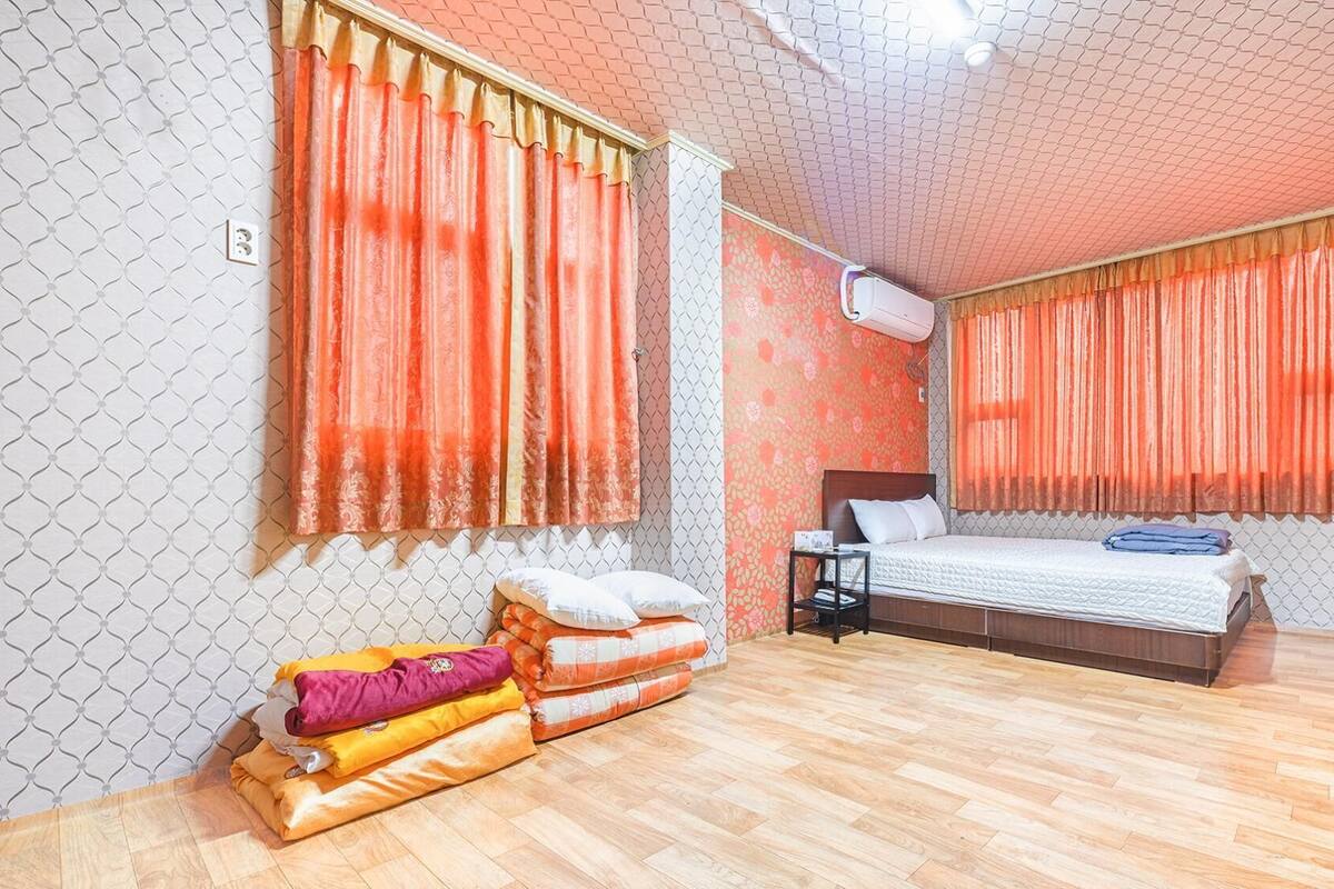 Una habitación de hotel con cama, una mesita de noche, un calentador y una ventana con cortinas.