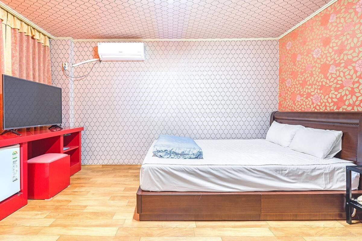 Habitación de hotel con cama, televisión, escritorio rojo con refrigerador y pared con diseño.