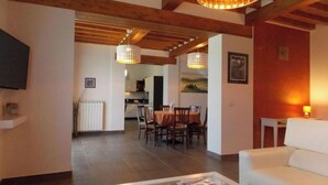 A spacious living area with a dining table, a sofa, and a glass coffee table. A kitchen is visible in the background. - Villa Moderna Grezzano (Grezzano)