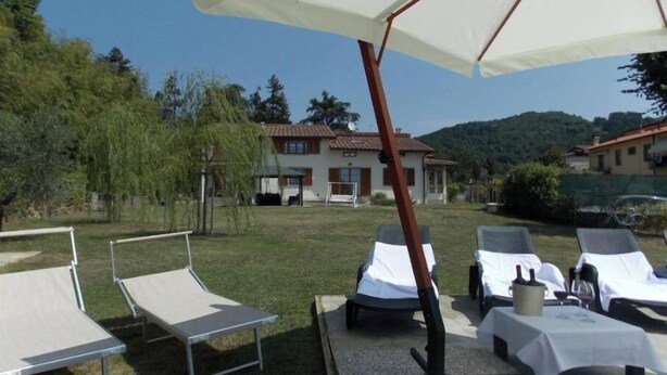 A patio with sun loungers and a large umbrella, surrounded by a grassy area and a house in the background. - Villa Moderna Grezzano (Grezzano)