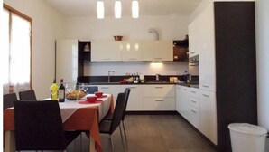 A compact kitchen with white cabinets, a dining table with chairs, and a trash bin. - Villa Moderna Grezzano (Grezzano)