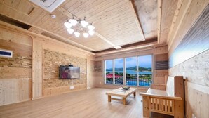 Una habitación amplia con paredes y suelos de madera, un ventanal con vistas, un banco de madera y una mesa con un cuenco.