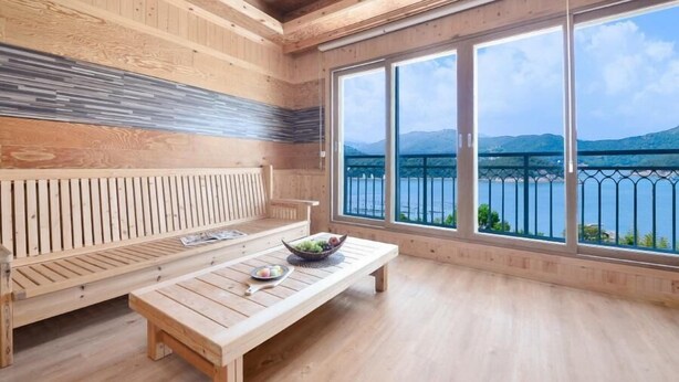 Un interior de madera con un banco, una mesa y ventanas amplias con vista a un lago.