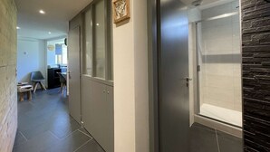 En hall med modern design, med en glasdörr som leder till ett badrum med en vägg av sten. I bakgrunden finns stolar och ett litet bord, vilket antyder ett väntrum eller en lounge.