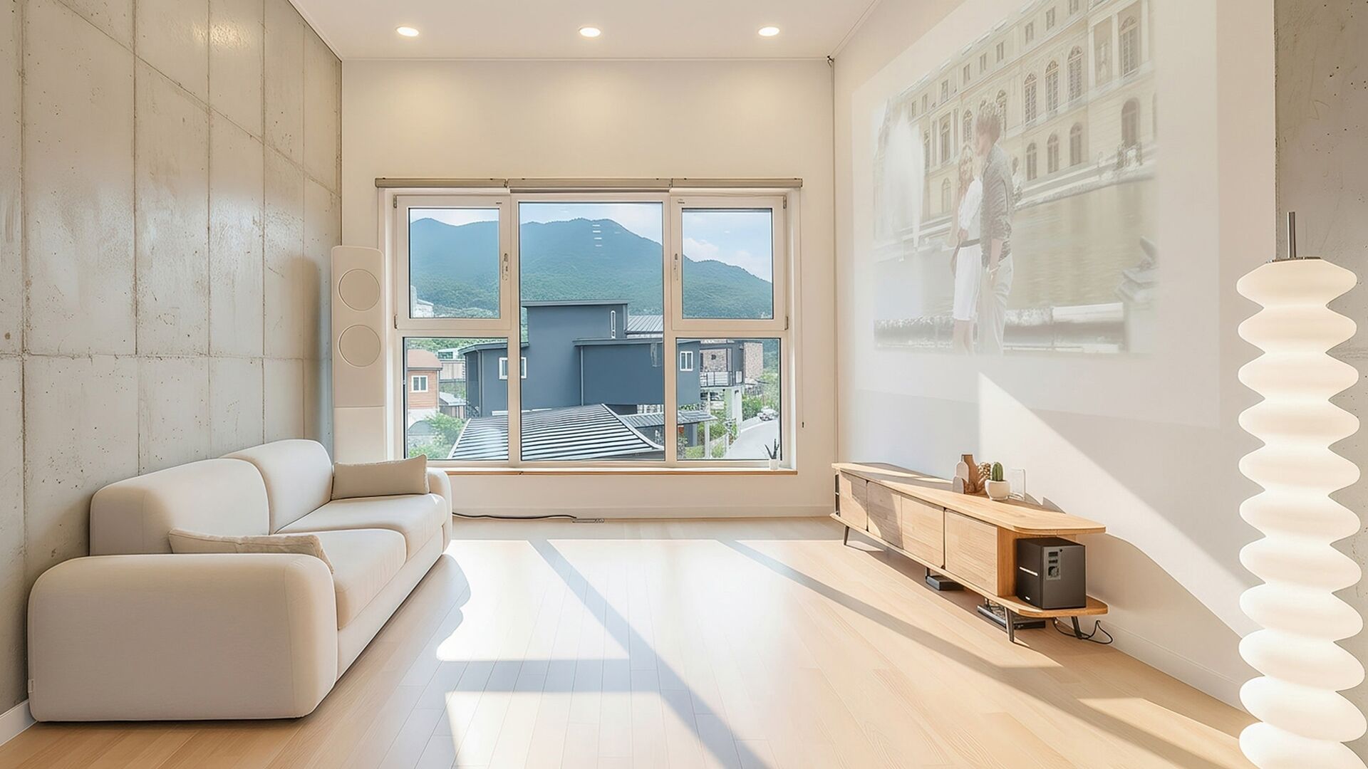 A modern living room with a sofa, a wooden cabinet, and a large window with a view of buildings and mountains.