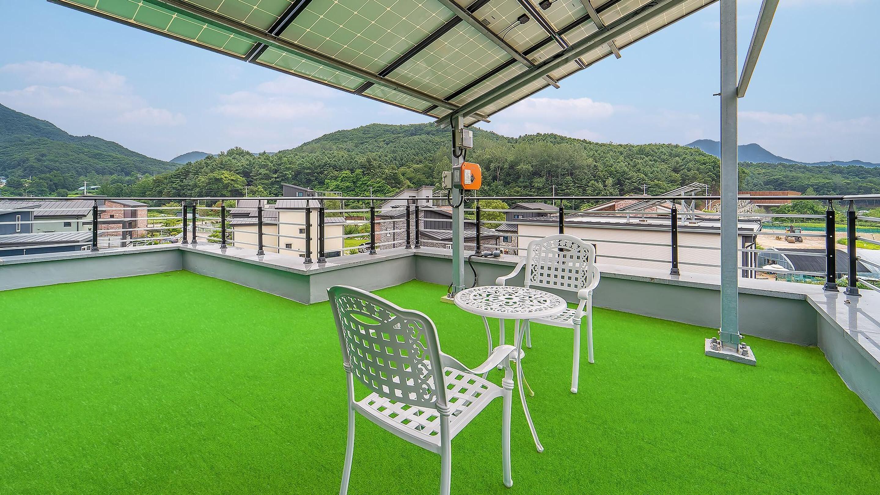 Une terrasse sur le toit, recouverte d’un gazon synthétique, avec deux chaises en métal blanc et une table.