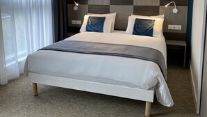 A modern hotel room with a large bed, a checkered headboard, bedside lamps, and sheer curtains. - Le Mitigana (Migennes)