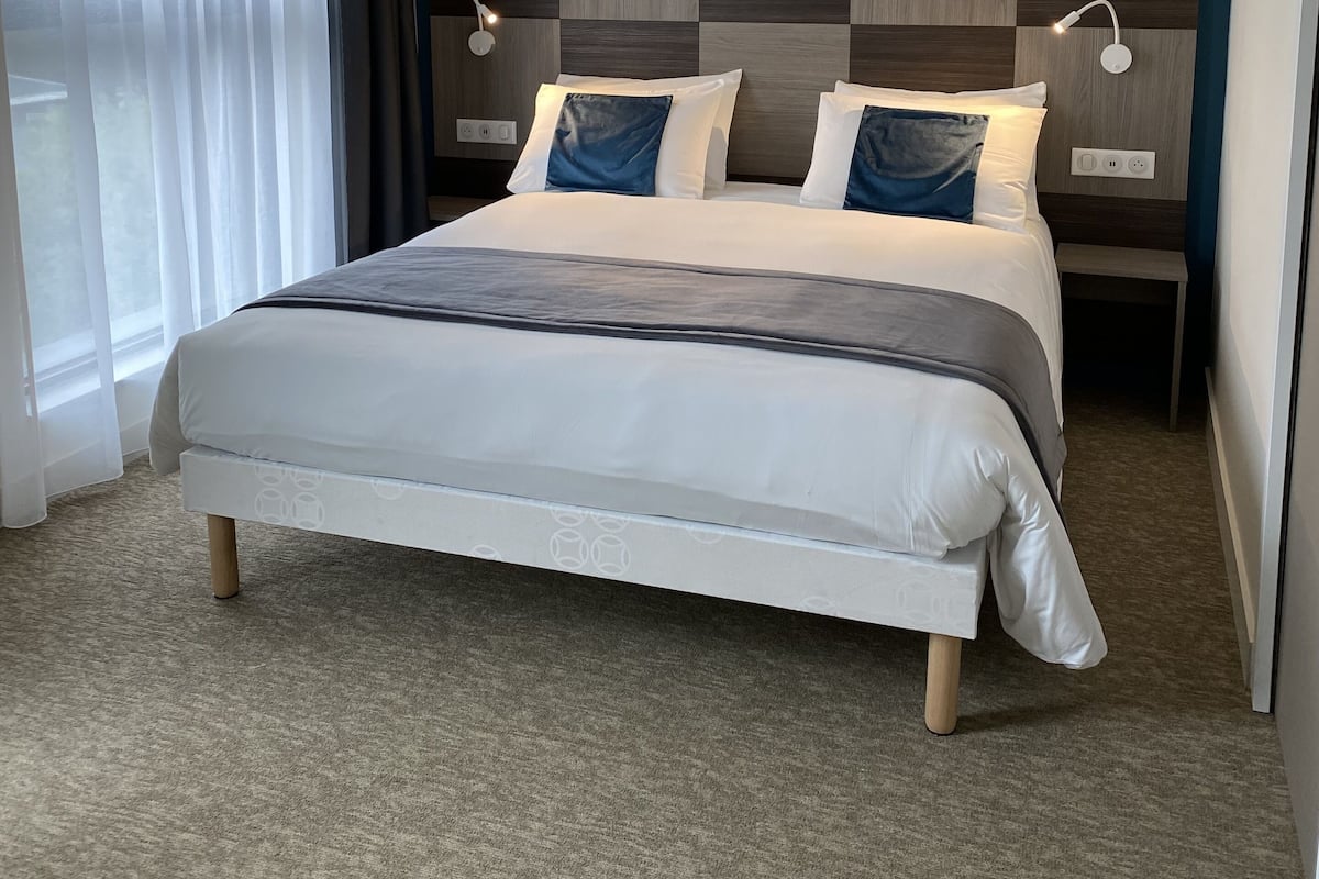 A modern hotel room with a large bed, a checkered headboard, bedside lamps, and sheer curtains.