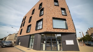 A modern building with a brick facade, large windows, and a ground-level entrance. - Le Mitigana (Migennes)