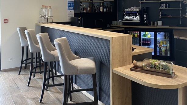 A bar area with a counter, stools, and overhead lighting. - Le Mitigana (Migennes)