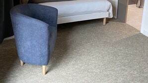 A modern hotel room with a large bed, a blue armchair, and a checkered headboard. - Le Mitigana (Migennes)