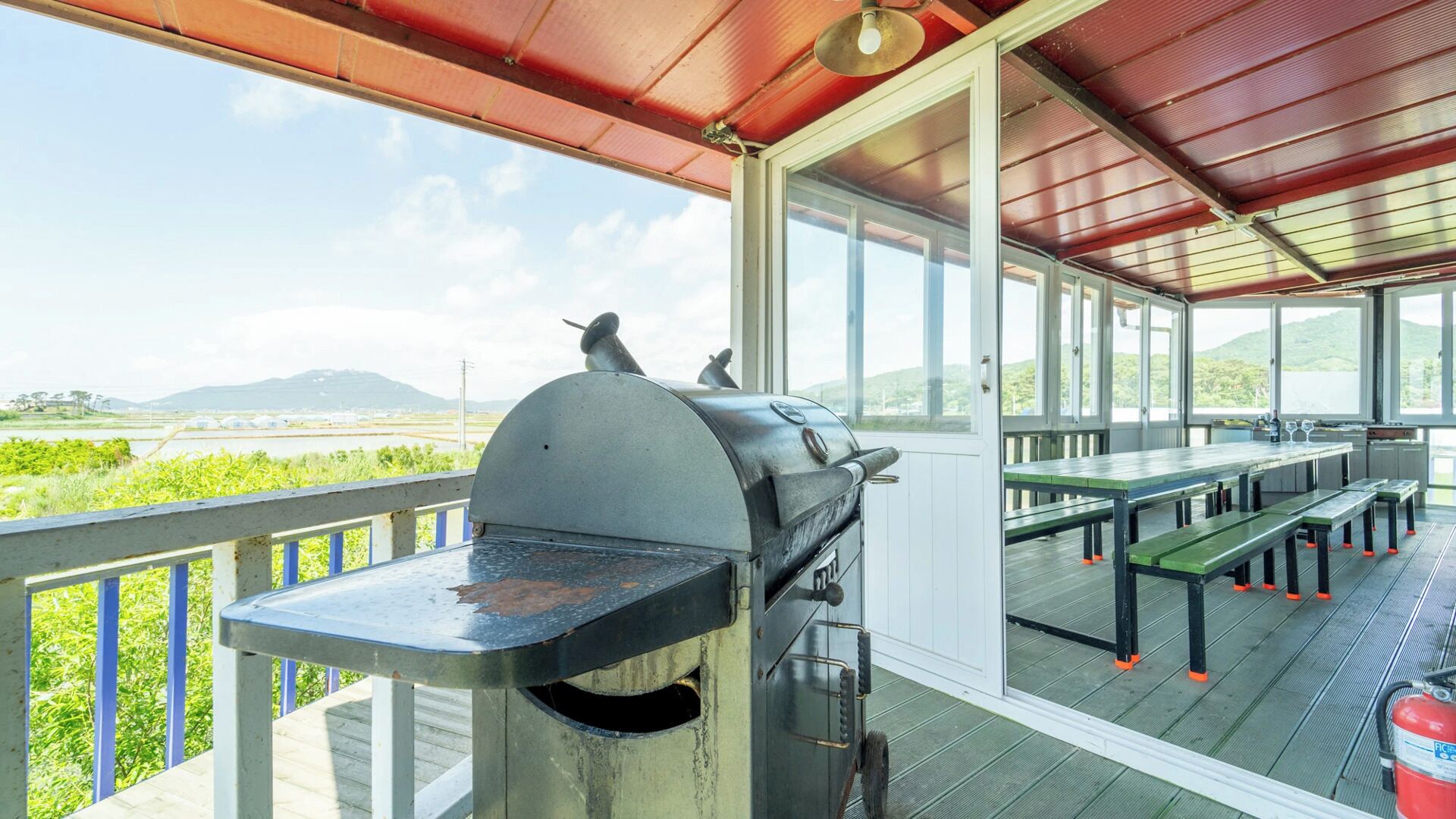 An outdoor patio with a grill, tables, and benches, overlooking a scenic landscape.