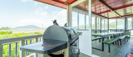 An outdoor patio with a grill, tables, and benches, overlooking a scenic landscape.