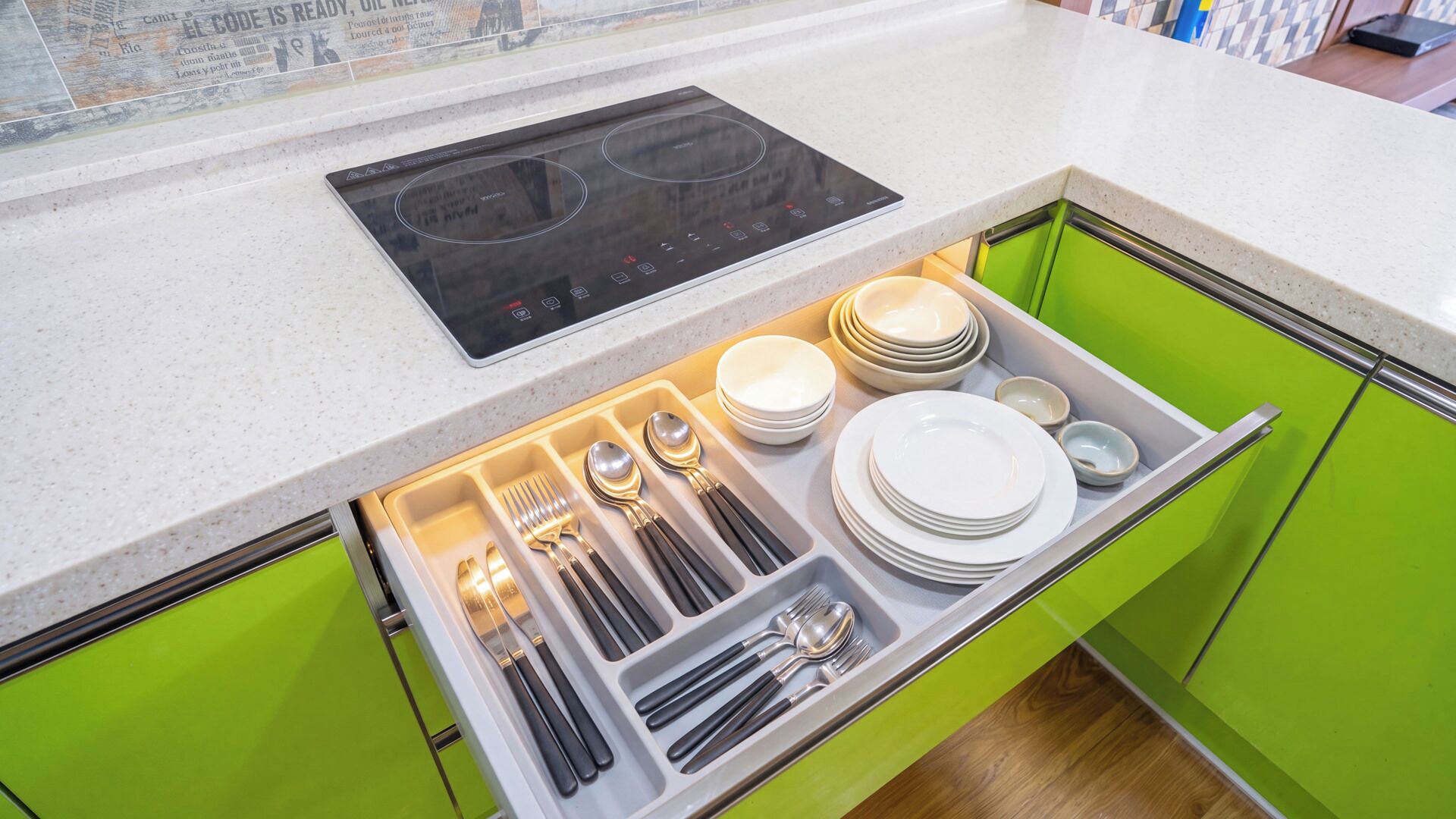 A kitchen with a built-in induction cooktop and a drawer organizer containing plates, bowls, and cutlery.