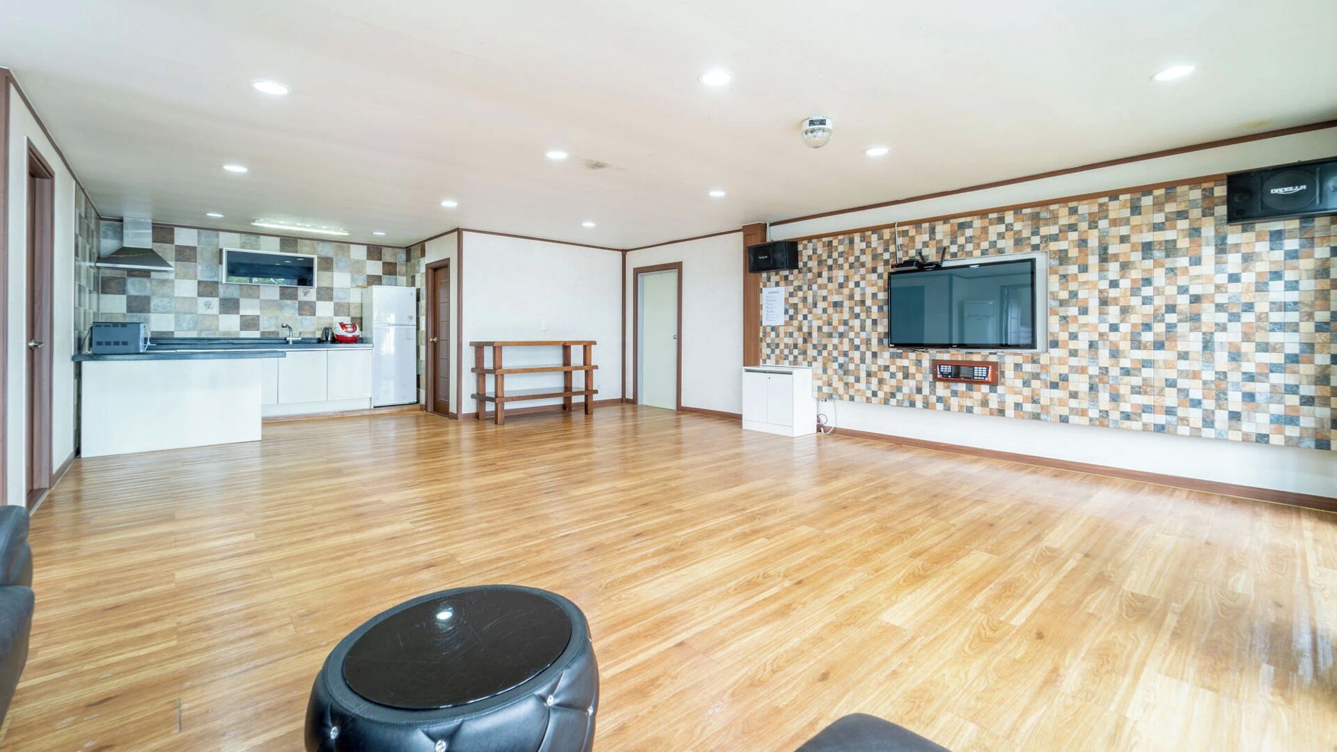 Amplia sala de estar con cocina, un televisor de pantalla plana en la pared y un banco de madera.