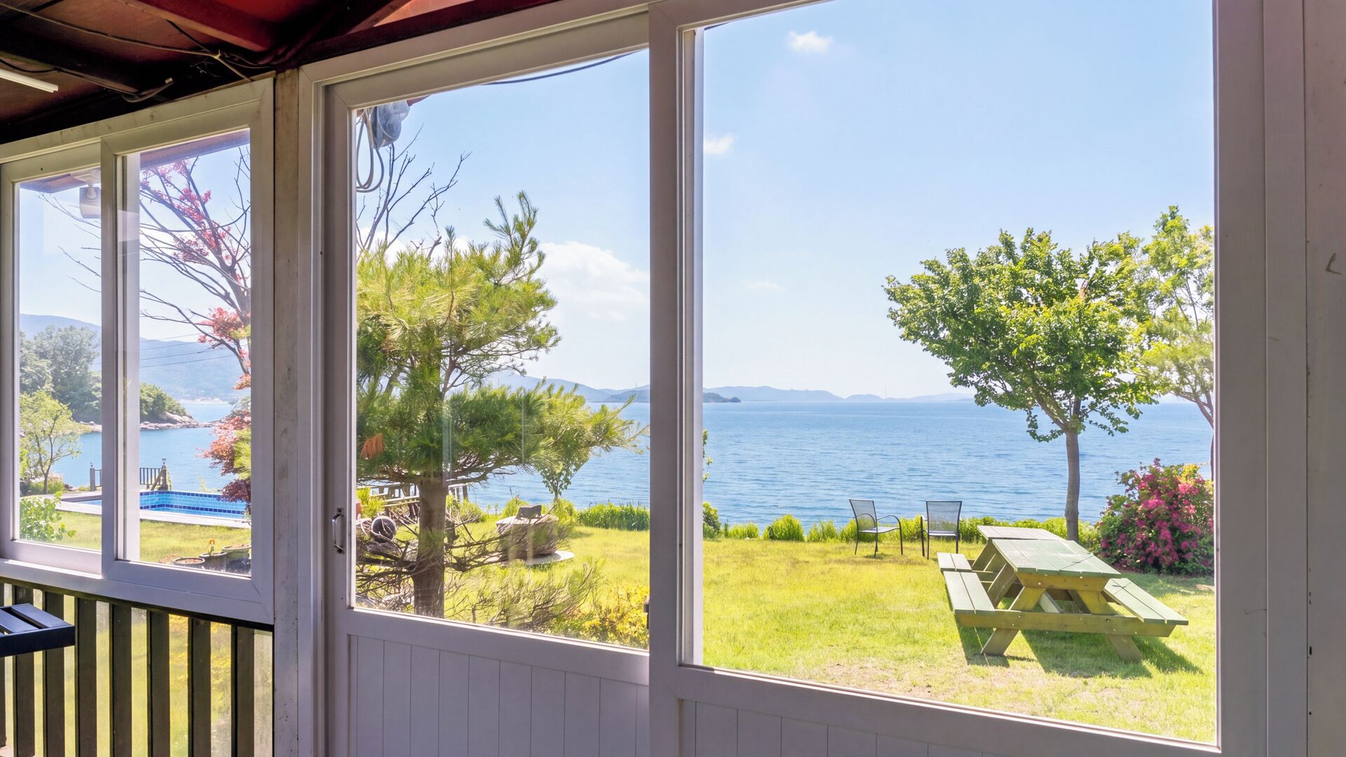 A covered outdoor area with large windows overlooking a grassy landscape and a body of water.