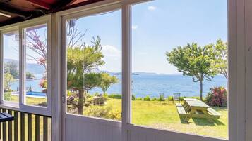 A covered outdoor area with large windows overlooking a grassy landscape and a body of water.