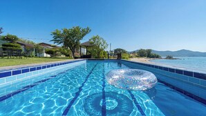 A clear blue swimming pool with a single inflatable ring, surrounded by a tiled deck and a view of the sea. - Ganghwa Badajeongwon Pension (Incheon)