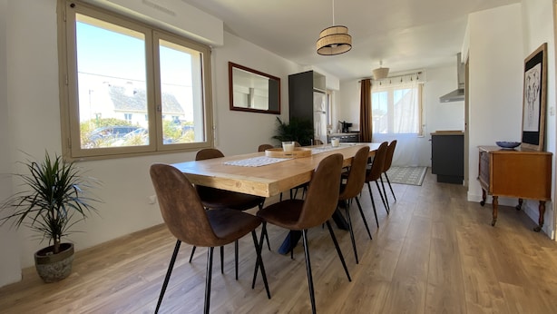 A dining area with a wooden table and brown chairs, a potted plant, and a view of the outside through large windows. - Holiday home, between bay and ocean (Saint-Pierre-Quiberon)