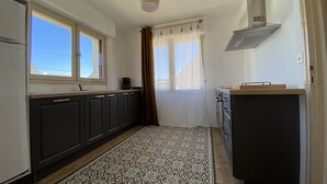 A compact kitchen with dark cabinets, a coffee maker, a stove, and a window with curtains. - Holiday home, between bay and ocean (Saint-Pierre-Quiberon)