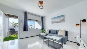 A modern living room with a sofa, coffee table, and a view of a balcony with a chair.