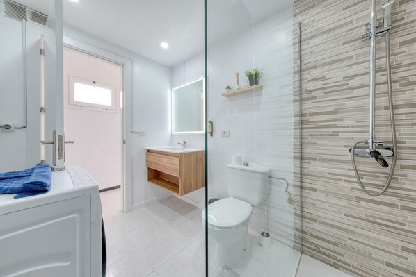 A modern bathroom with a glass shower enclosure, a toilet, and a sink with a mirror above it. - Suite Helios • 500M from the beach • LVH (Puerto del Carmen)