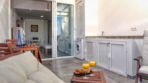 Un salon moderne avec un canapé, une table basse en bois sur laquelle sont posés des croissants et un jus d’orange, un coin repas avec une table et des chaises, un lave-linge et une porte vitrée donnant sur un balcon.