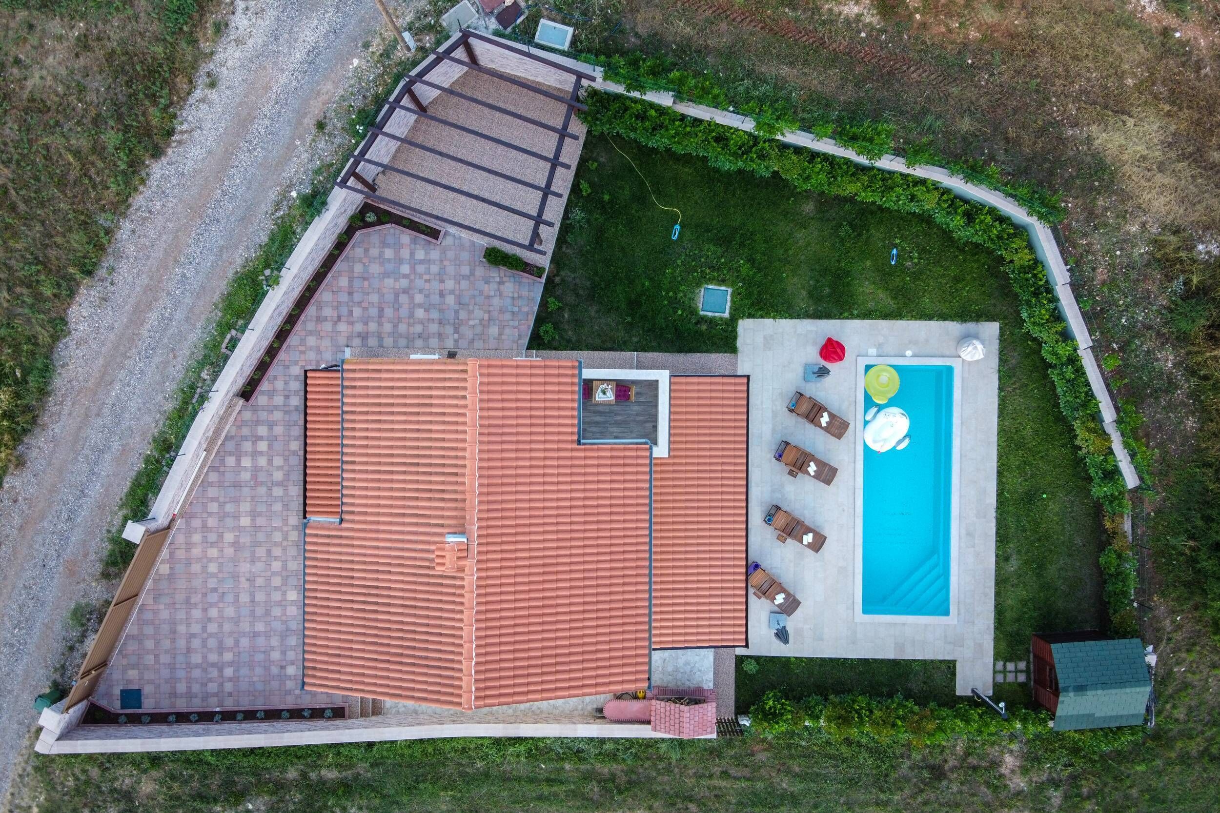 Eine Luftaufnahme eines Hauses mit Swimmingpool, einer Terrasse mit Sitzgelegenheiten und einem überdachten Außenbereich.