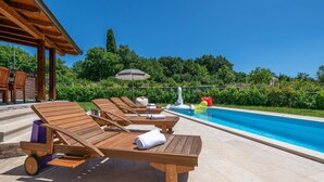 Ein Poolbereich mit Holzliegen, einer überdachten Sitzgelegenheit und freiem Blick auf den Pool.