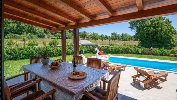 Eine Terrasse im Freien mit einer Holz-Pergola, einem Esstisch und einem Pool im Hintergrund.