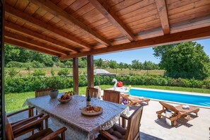 An outdoor patio with a wooden pergola, a table set for dining, and a pool in the background. - Villa Madonnina with pool (Manjadvorci)