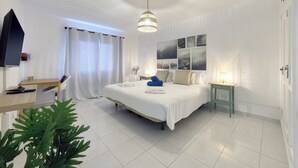 Ein modernes Hotelzimmer mit einem großen Bett, einem Schreibtisch, einem Sessel, einem kleinen Tisch, einer Pflanze und einer Wand mit Bildern.