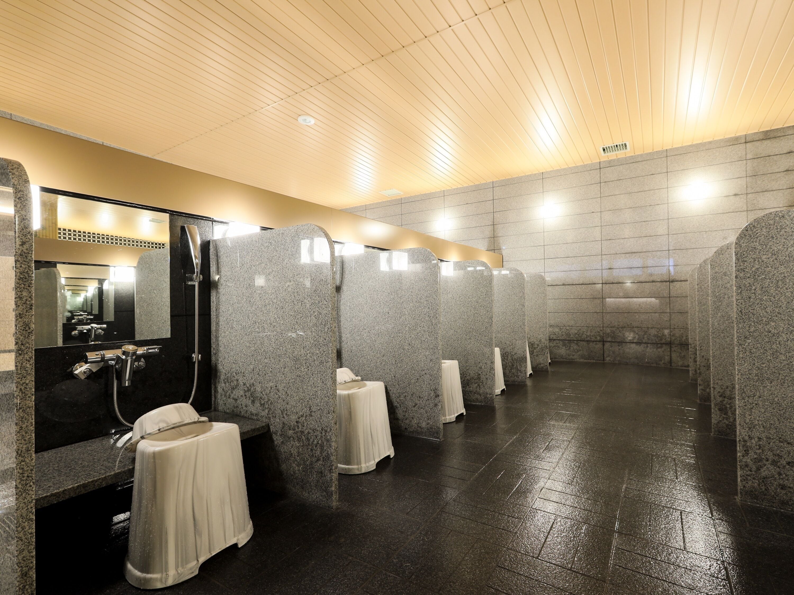 A public restroom with granite partitions, a black sink, and a mirror.
