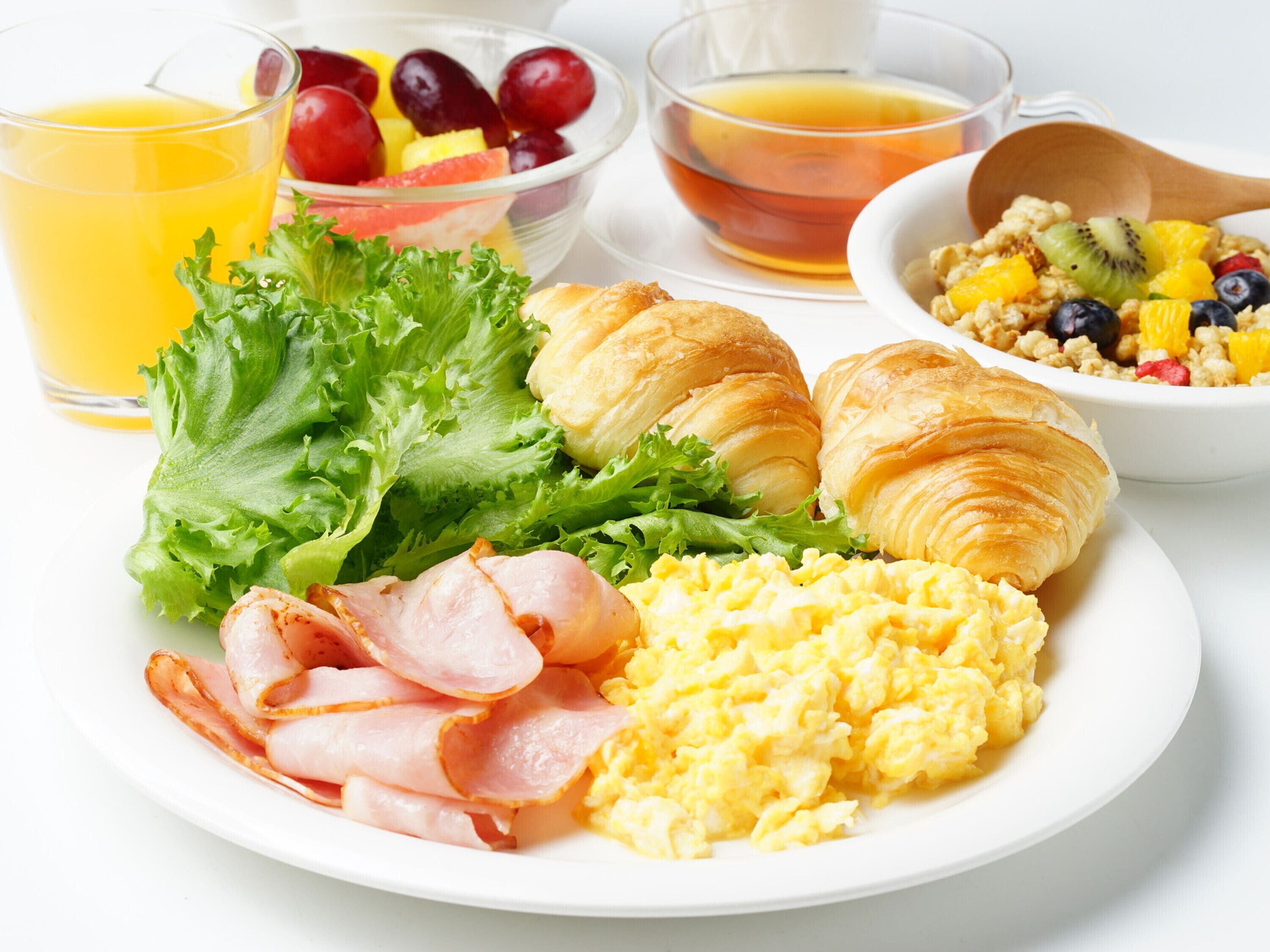 Un piatto per la colazione con uova, pancetta, croissant e un'insalata.