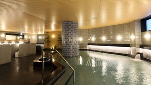 Un área de piscina interior moderna con un elemento central de agua, asientos a lo largo de las paredes y un techo de madera.
