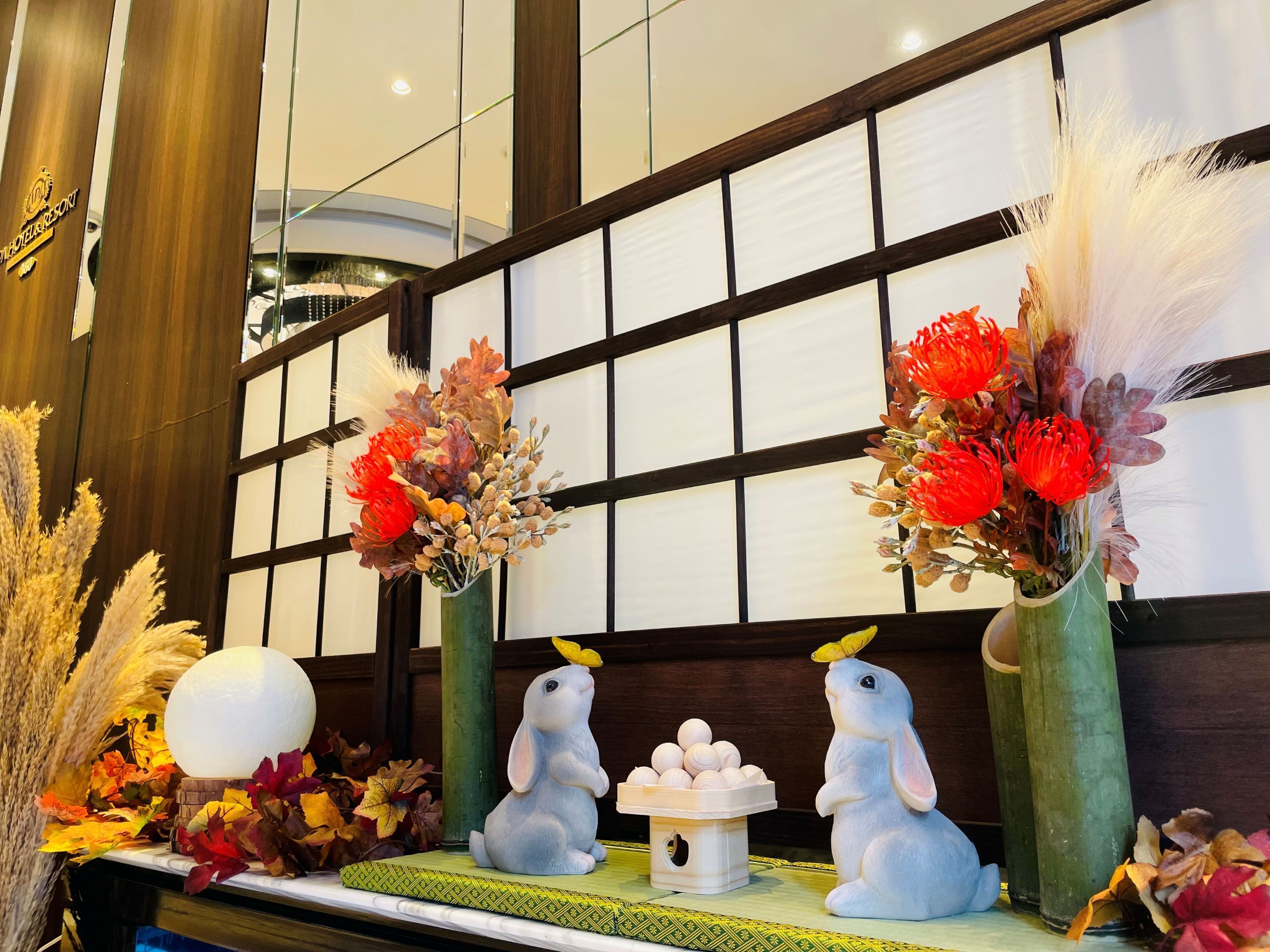 A decorative display with flowers, a white spherical object, and two rabbit figurines.