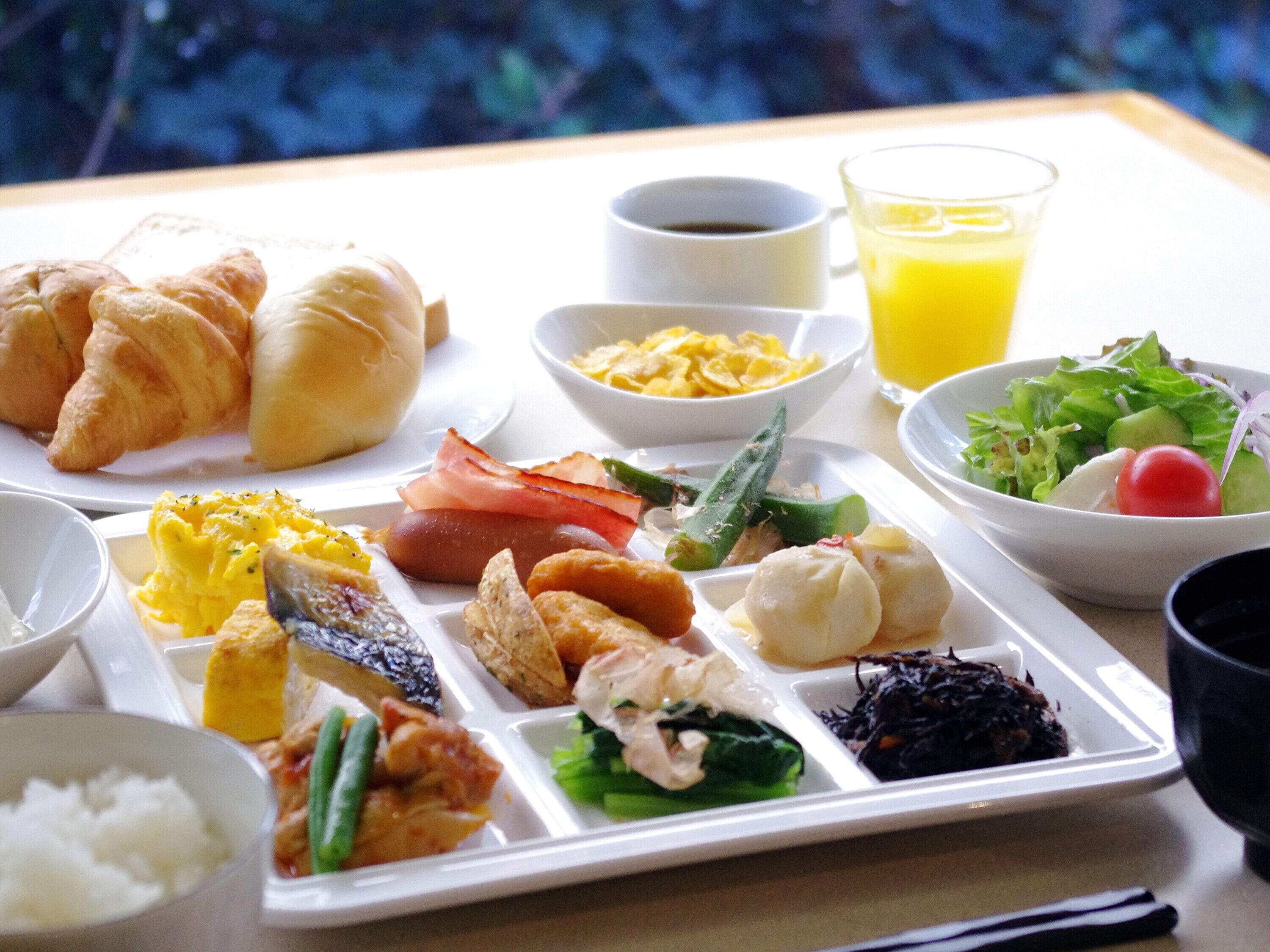 Un plateau repas contenant divers plats, notamment des croissants, des œufs, des saucisses et des légumes.