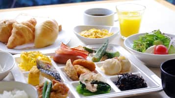 Un plateau repas contenant divers plats, notamment des croissants, des œufs, des saucisses et des légumes.