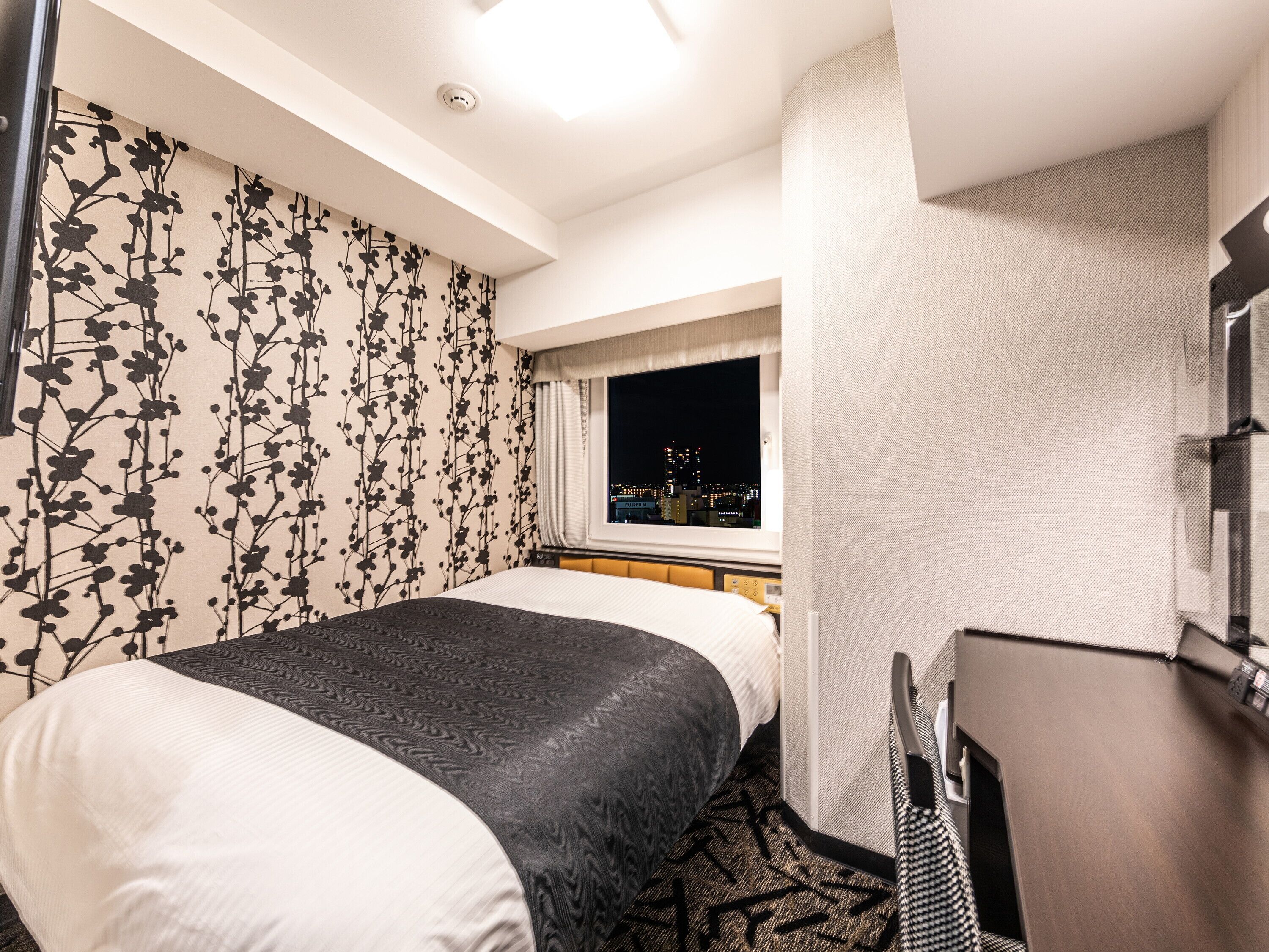 Una habitación de hotel con cama, escritorio, ventana y vista a la ciudad, y pared con diseño.