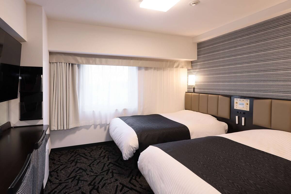 Une chambre d’hôtel avec deux lits, un téléviseur à écran plat, une fenêtre avec des rideaux et un luminaire au plafond.