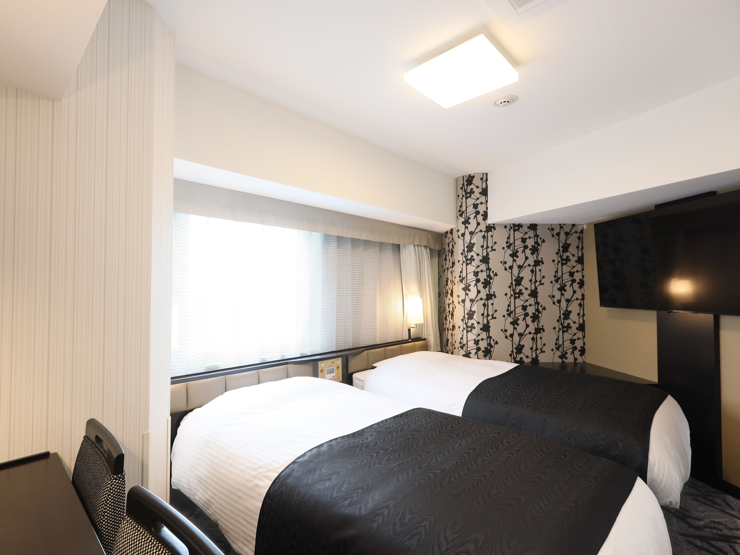 A hotel room with two beds, a desk, and a TV.