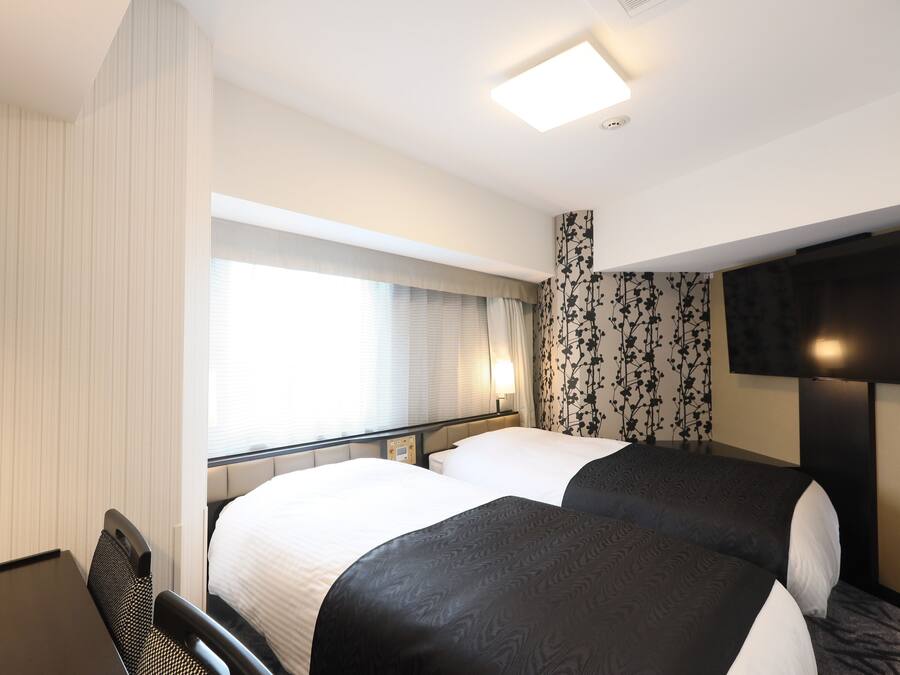 A hotel room with two beds, a desk, and a TV.