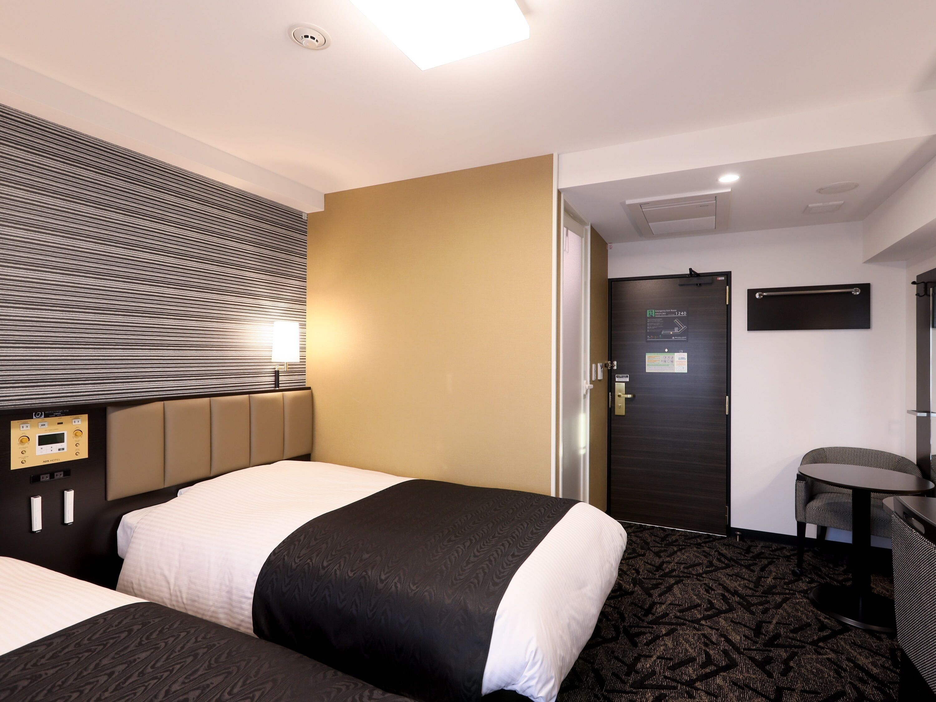 Ein Hotelzimmer mit zwei Betten, einer Steuerung, einem Schreibtisch und einer Tür mit einem Schild.