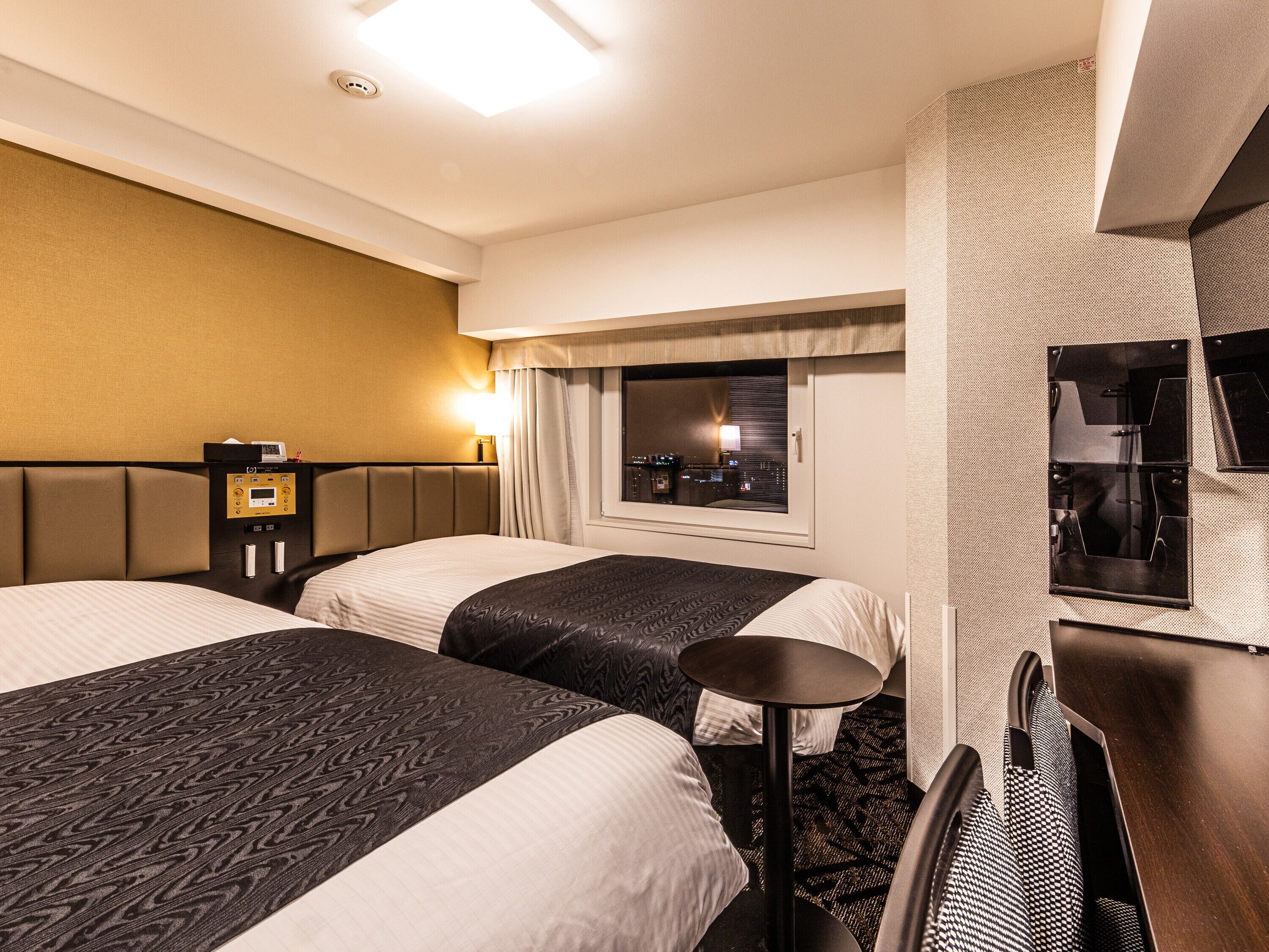 A hotel room with two beds, a small table, a TV, and a window with a city view.